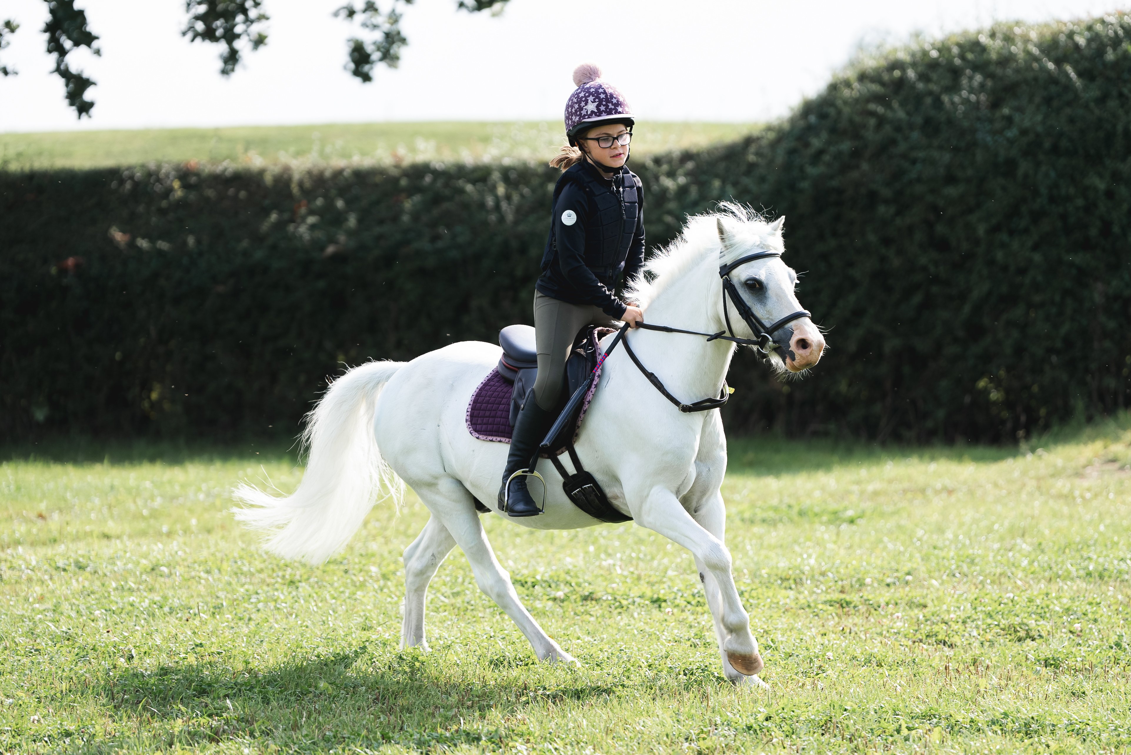 Child riding a pony wearing a helmet and body protector.